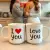 Photo : Deux mugs "I Love You" côte à côte sur une table de cuisine, avec des cœurs en arrière-plan
