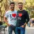 Un homme souriant, peut-être avec sa partenaire, tous deux portant le tee shirt "love you" dans un cadre décontracté comme un parc ou un café.