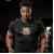 Un jeune homme musclé, portant le T-shirt de sport noir, effectuant une séance de musculation intense. Son visage est concentré, le t-shirt met en valeur sa musculature tout en restant sec.