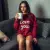 Une jeune femme, assise confortablement sur un canapé, buvant un thé dans un mug, portant le sweat à capuche "I love you" couleur bordeaux. Ambiance cozy, lumière douce.