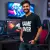un homme souriant, portant le t-shirt noir "Geek", assis devant un setup de gaming stylé